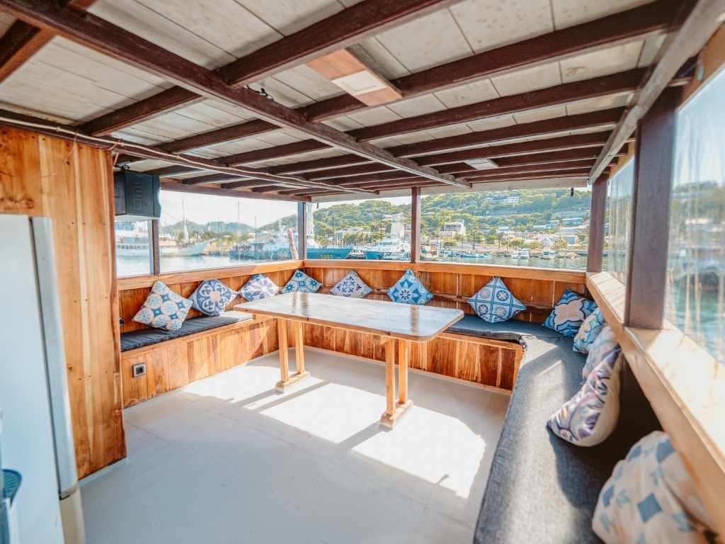 Ruang Santai Kapal Pesona Bajo: Area Makan Tertutup dengan View Pelabuhan Labuan Bajo